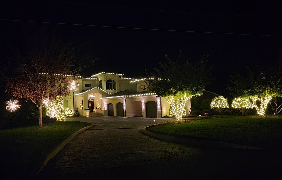 Large estate with roofline lights, wrapped trees, lit bushes and spritzers
