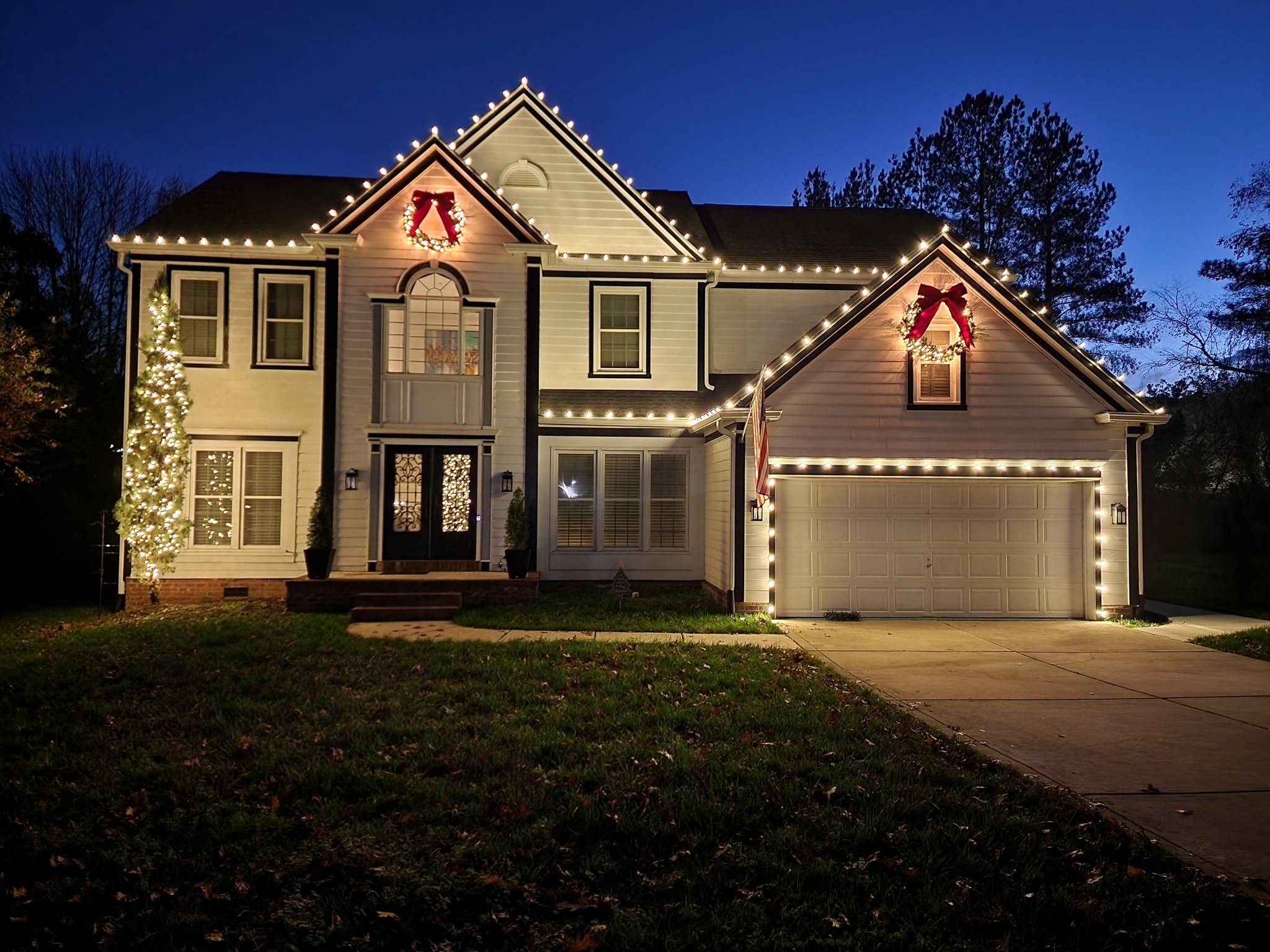 Large two-story home with roofline lighting, wreaths and a wrapped tree