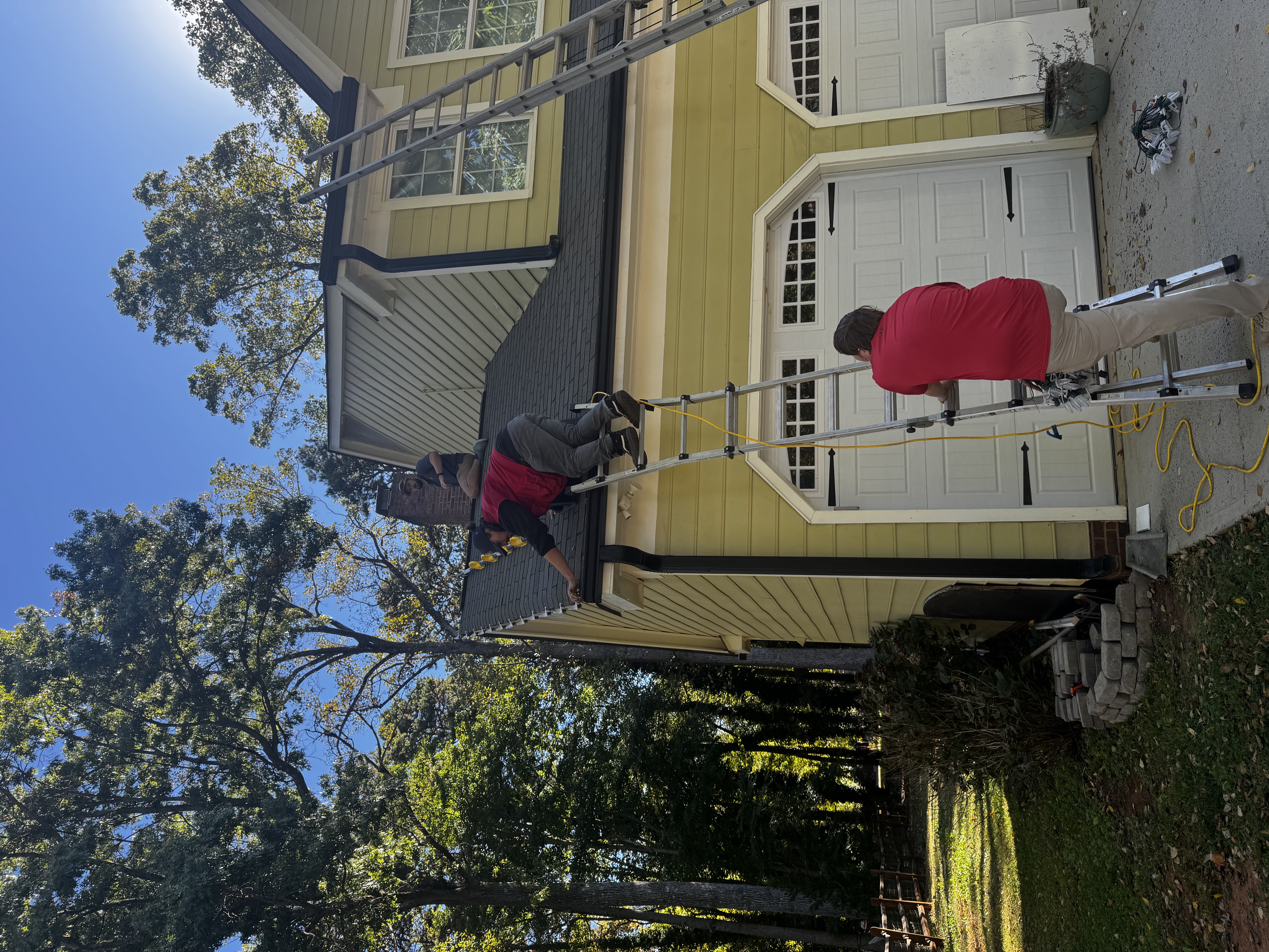 Installation team practicing Christmas light work from ladders and a roof